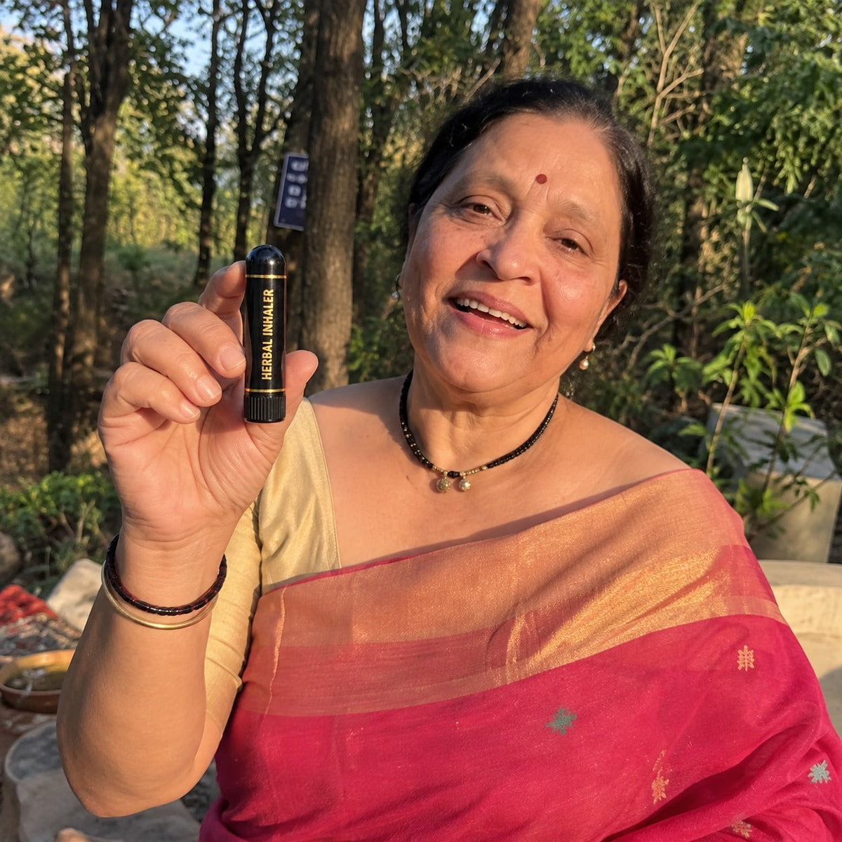 Smiling woman in a red saree holding the Sugar Balance Inhaler outdoors